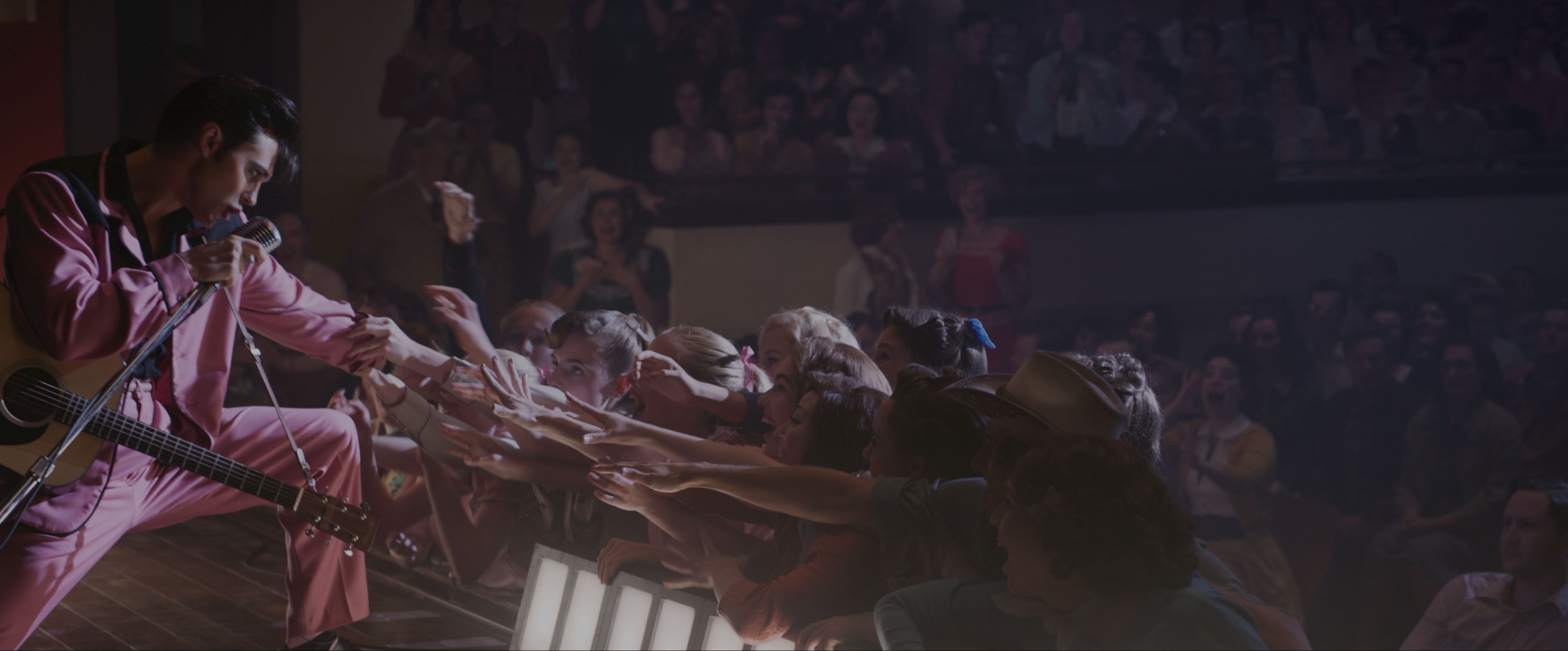 An actor dressed as Elvis Presley reaching into a crowd. 