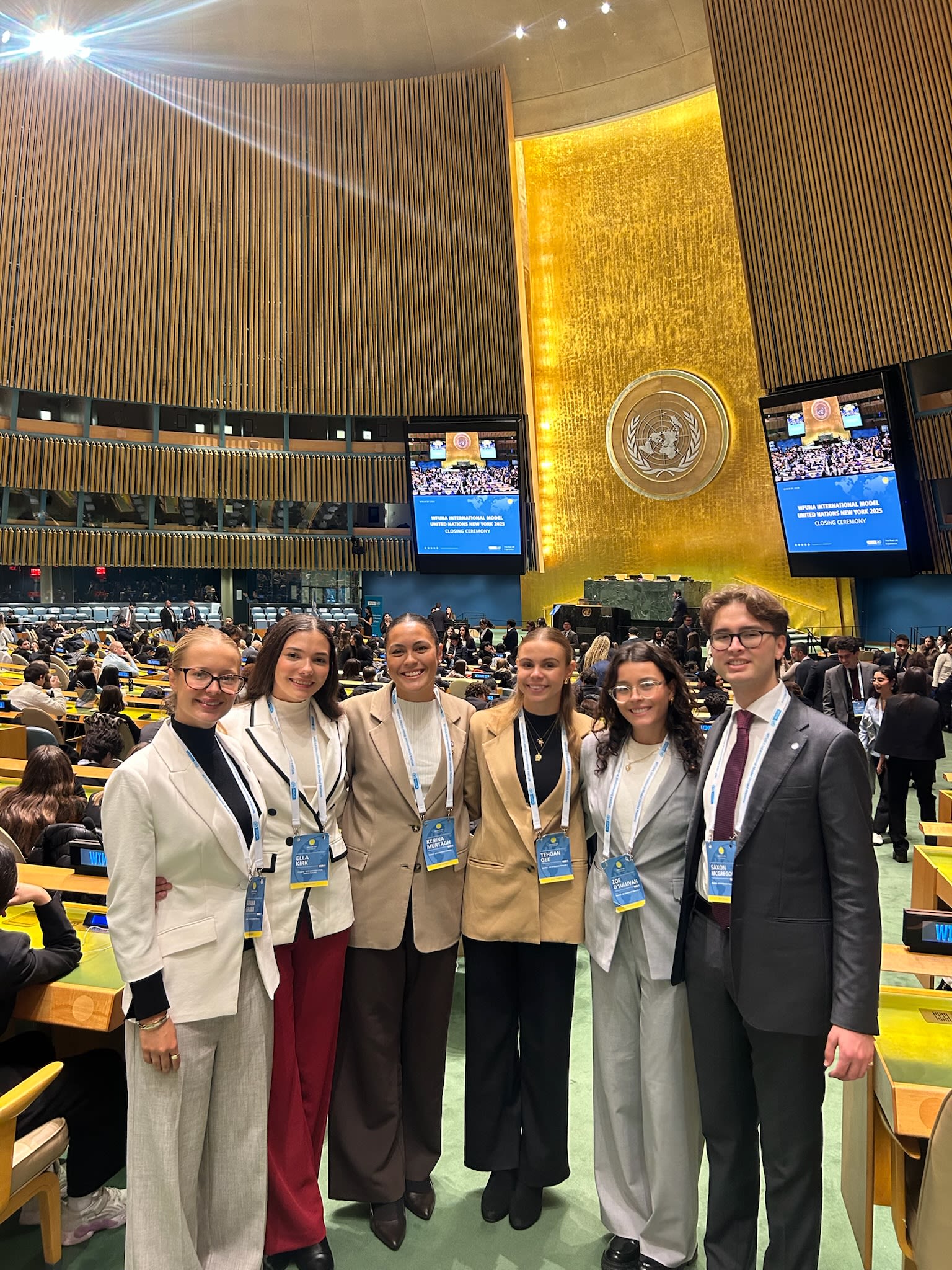 Students are sat at a conference table with United Nations imagery behind them.