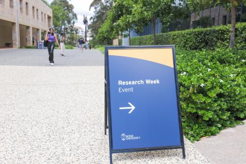 A sign which reads "Research Week Event" is placed on a footpath outside the HSM Faculty. 