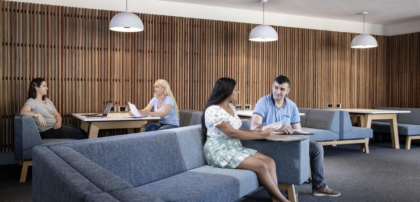 Four students sitting in a Bond Business School study area with their laptops and textbooks open on the desks.