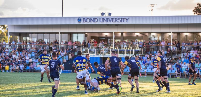 Men's rugby game whilst spectators watch from the stands.