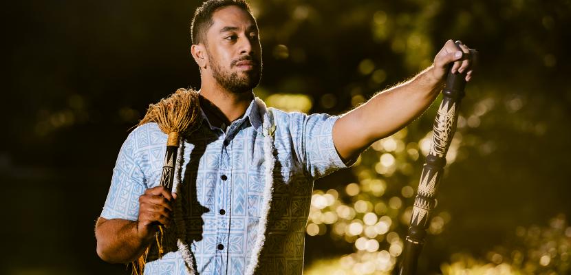 Alumnus Dr Dion Enari wearing a blue shirt and holding a bamboo torch