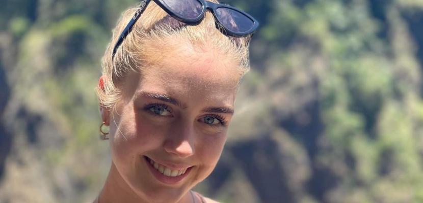Michaela Wilson, a white woman with blonde hair, smiles at the camera with nature in the background
