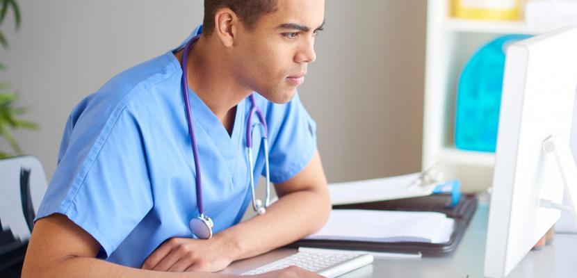 A person dressed in scrubs with a stethoscope around thier neck is working at a computer