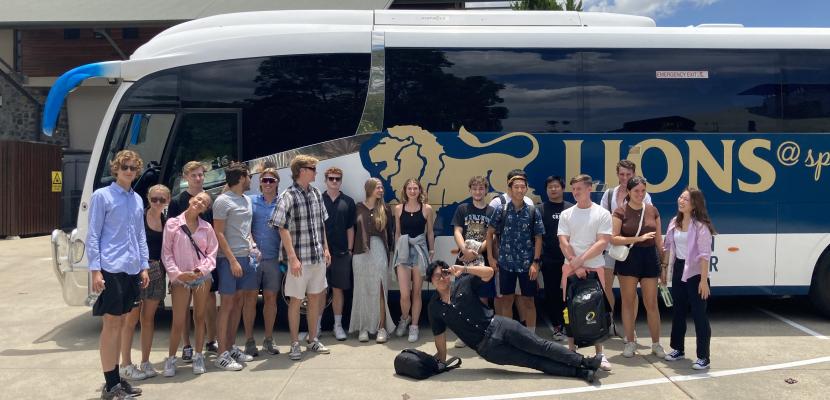 A group of students stand in front of a bus smiling