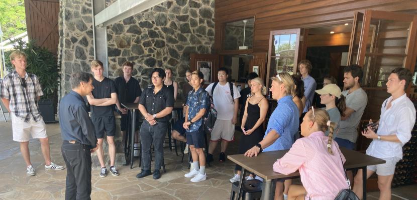 A group of around 15 students stand around in a circle watching a presentation at Sirromet Winery