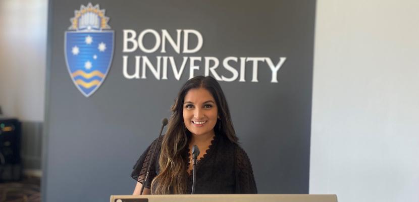 Aaliyah Mohammed stands at a podium in a classroom, in front of a Bond University sign