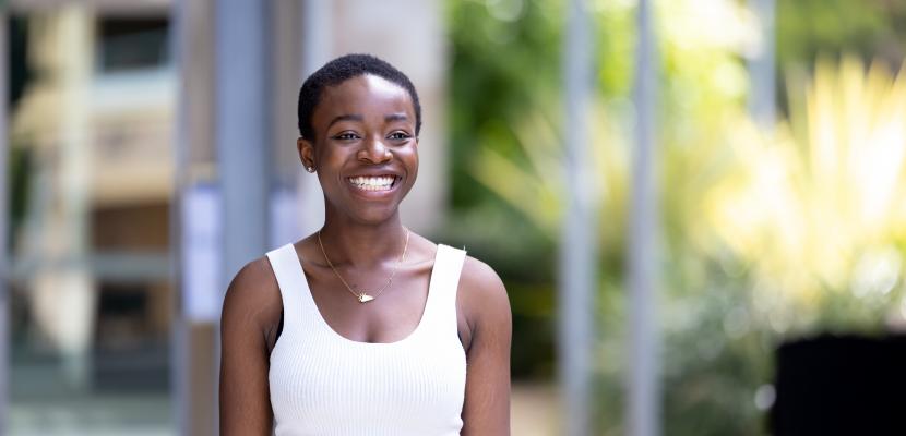 Ma-Janneh Miller, a Black woman with short dark hair, stands towards and smiles broadly
