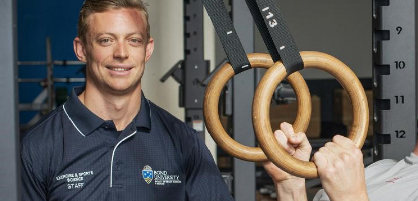 Robbie Palmer smiles facing the camera next to gym equipment