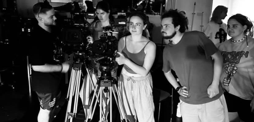 Anna Pata and a group of students stand behind a tripod and camera in black and white
