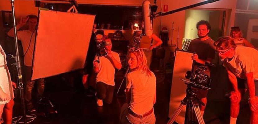 A group of people stand in front of a screen in a red room using film equipment