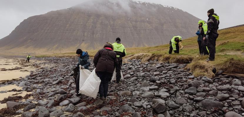People walk along a misty beach collecting debris into heshan bags.