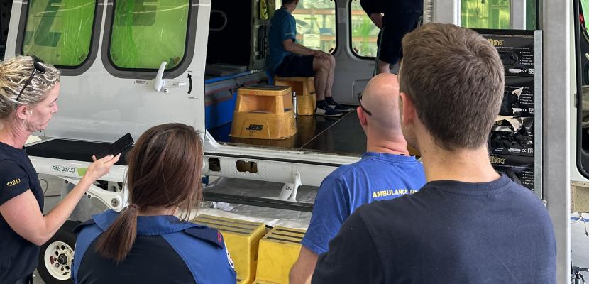 Four people are standing outside of a grounded rescue helicopter and looking in.