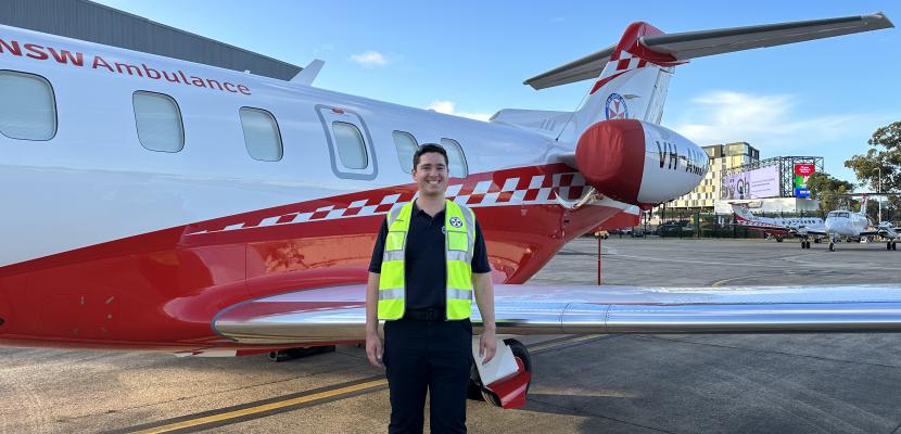 A young man is standing in front of an airplane in high-visibility clothing. 