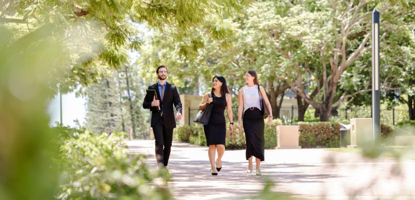 Three students are walking down a path surrounded by trees.