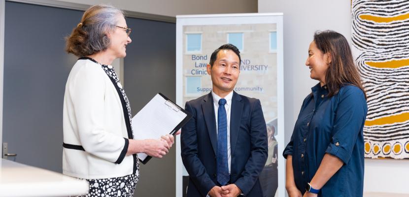 Three people in corporate attire are standing in a circle talking and smiling. 