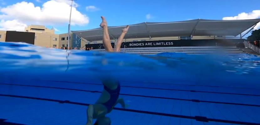 A woman is pictured half in and out of the water, in an artistic swimming routine in a pool. 