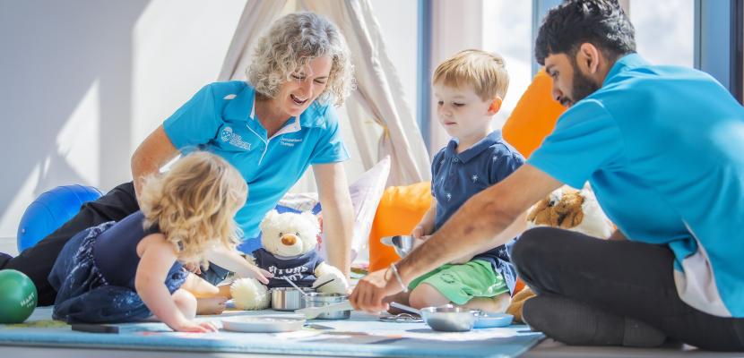 An Occupational Therapy student and a teacher sitting on the floor and playing with two small children