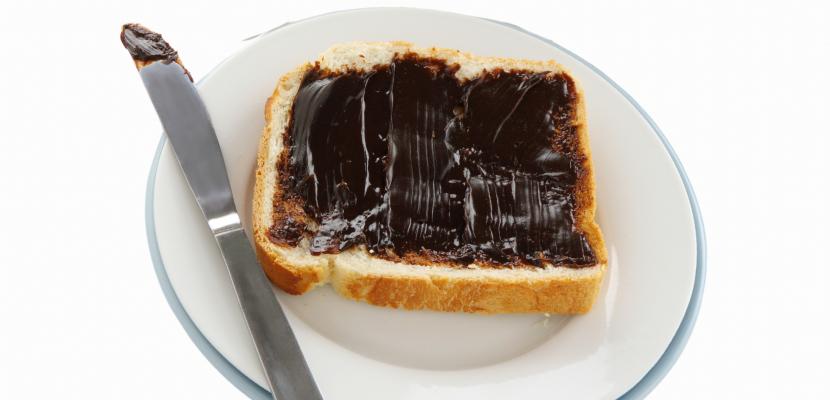 Slice of toast on a plate with thickly-spread vegemite next to a knife