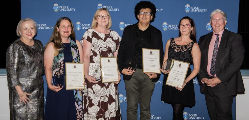 Six people standing together in front of a Bond University banner holding framed awards