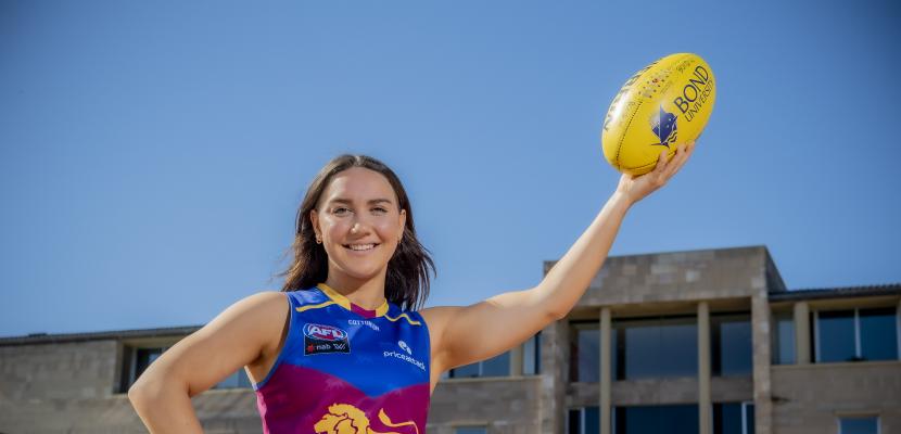 Womens AFL star Mikayla Pauga holding an Aussie rules football in the air in front of the Arch.