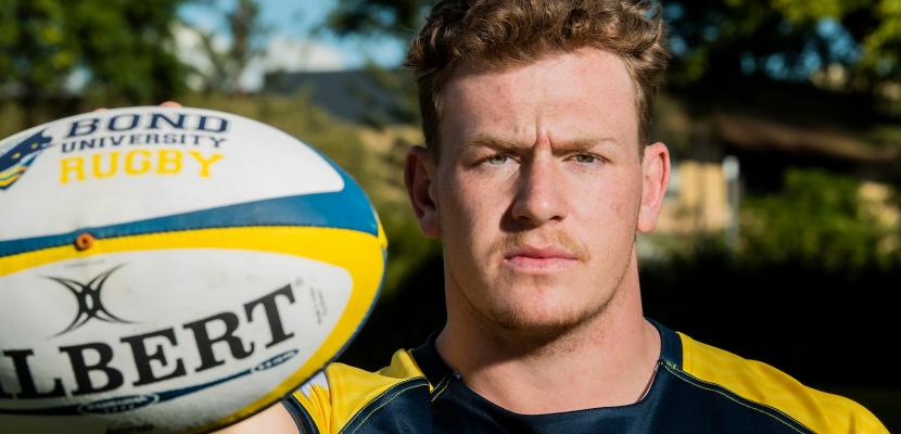 Man holds a rugby ball in one hand for a photo