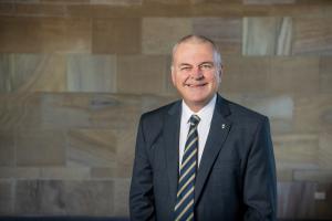 Vice Chancellor Tim Brailsford smiling at camera with tiled sadnstone background.