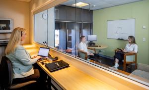 Female behind a glass screen watching a female psychologist interact with her client.