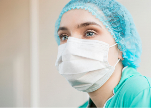 A doctor is wearing a face mask and hair net looking off in the distance