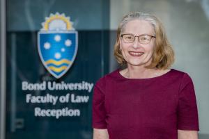 A portrait of a woman smiling, standing in front of a door that reads Bond University Faculty of Law