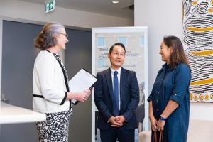 Three people in corporate attire are standing in a circle talking and smiling. 