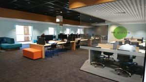 A large room with desks and computers. There is an ottoman and other soft seating