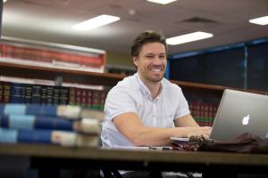 A person sits at a desk in the law library on a laptop smiling